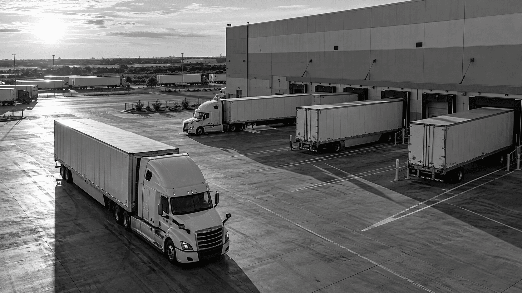 Illustrative black-and-white scene of tractor-trailers at a freight terminal's loading docks.